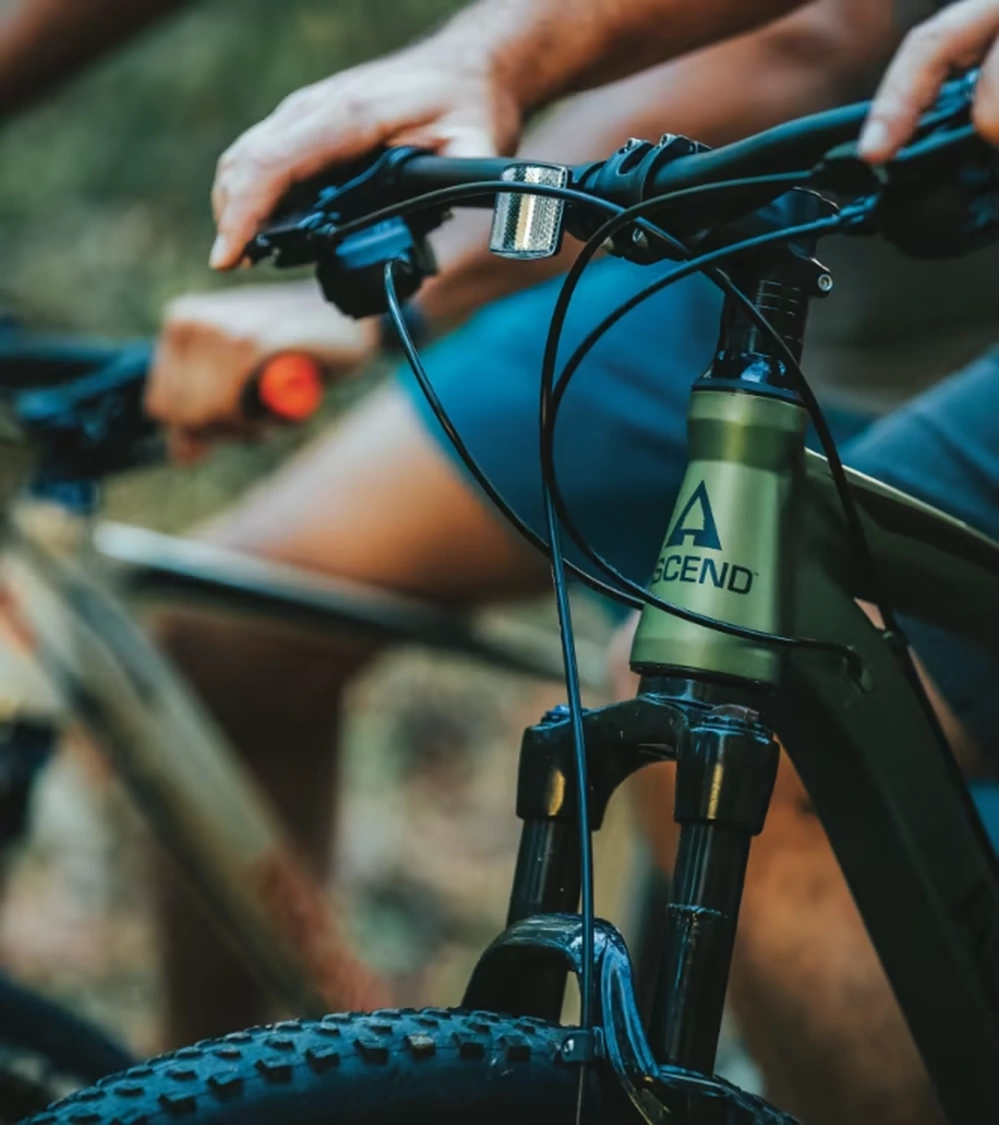 Close view of a green Ascend bicycle frame, logo and front suspension with a rider behind it.